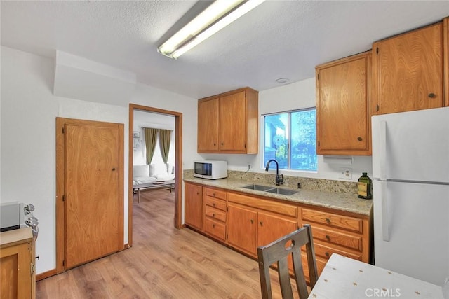 kitchen featuring white appliances, sink, a textured ceiling, and light wood-type flooring