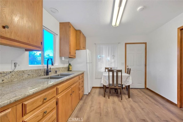 kitchen featuring white fridge, sink, light stone counters, and light wood-type flooring