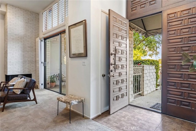 doorway to outside with light colored carpet, brick wall, and a high ceiling