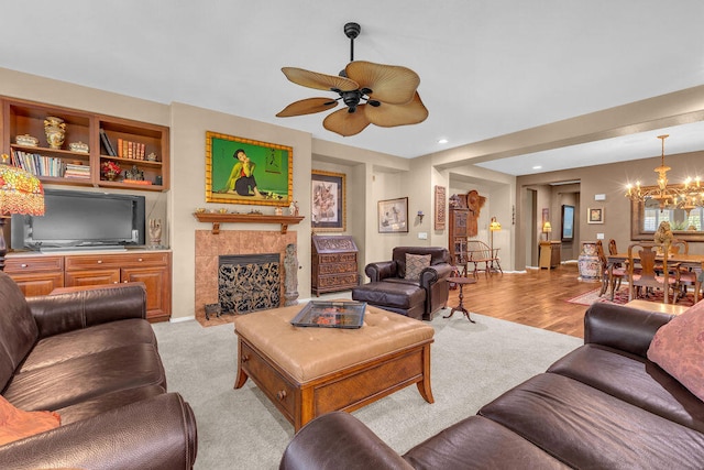 living room with built in shelves, ceiling fan with notable chandelier, and a tile fireplace