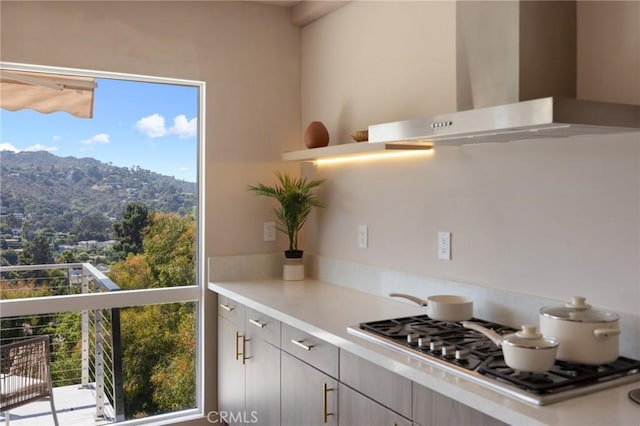 kitchen with wall chimney range hood, stainless steel gas stovetop, and light countertops