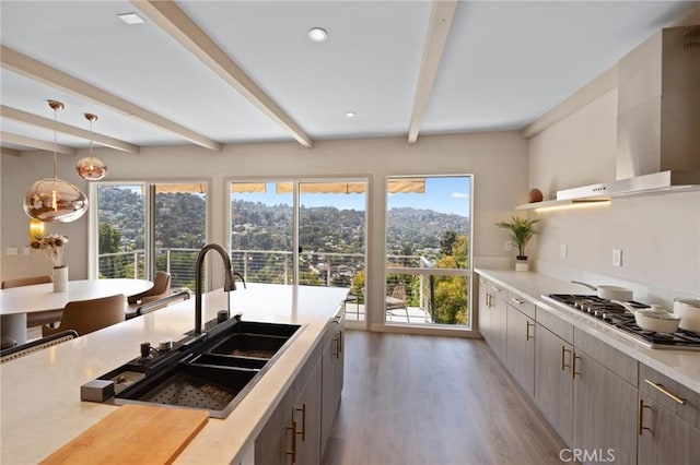 kitchen with stainless steel gas cooktop, a sink, light wood-type flooring, beamed ceiling, and wall chimney exhaust hood