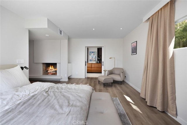 bedroom featuring recessed lighting, visible vents, wood finished floors, a lit fireplace, and baseboards