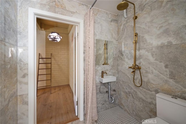 bathroom with toilet, a tile shower, and tile walls