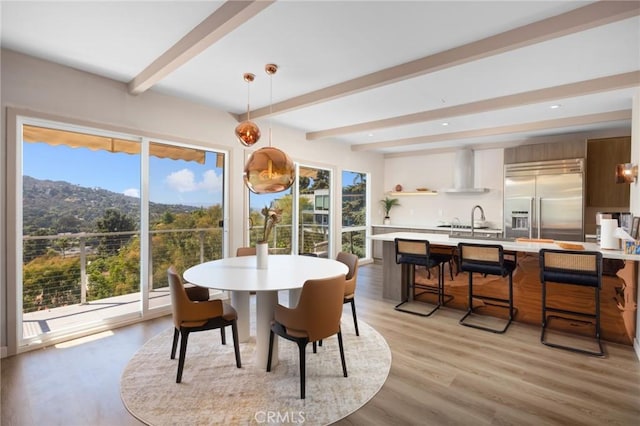 dining space featuring light wood-type flooring and beamed ceiling