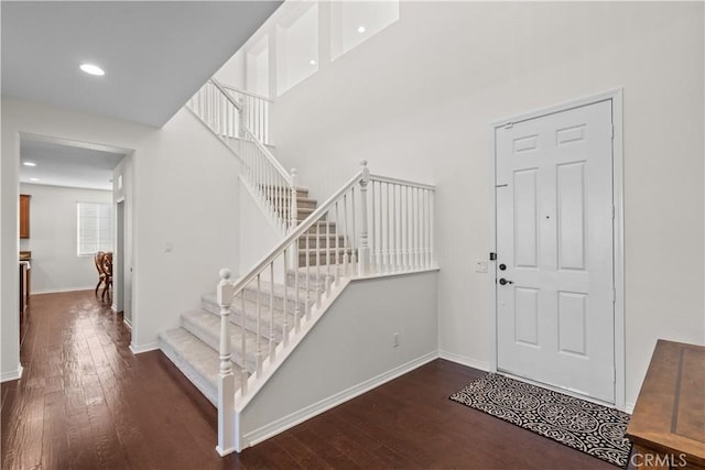 foyer featuring baseboards, a towering ceiling, hardwood / wood-style floors, stairs, and recessed lighting