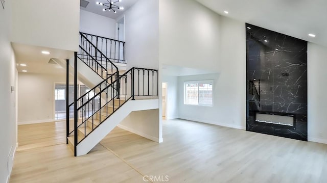 foyer entrance with light wood-type flooring, a chandelier, a towering ceiling, and a fireplace