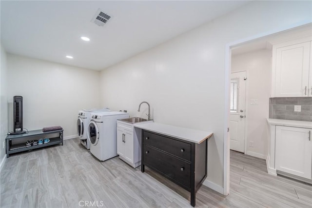 washroom featuring light hardwood / wood-style floors, sink, washing machine and dryer, and cabinets