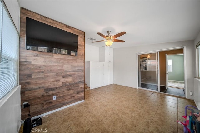 unfurnished living room featuring ceiling fan and wood walls