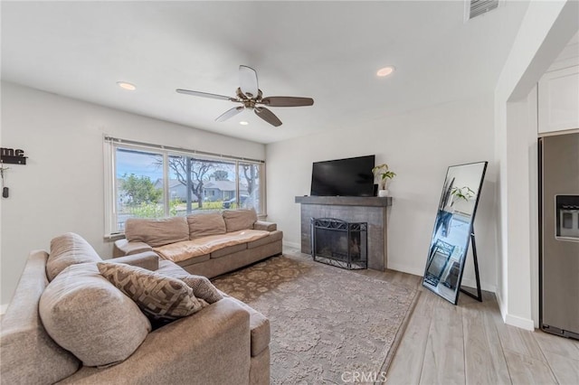 living room with ceiling fan, light hardwood / wood-style floors, and a tile fireplace