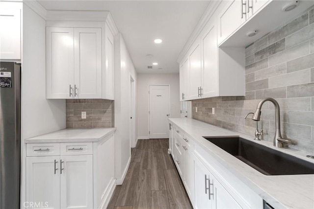 kitchen featuring sink, stainless steel fridge, white cabinets, dark hardwood / wood-style flooring, and light stone countertops