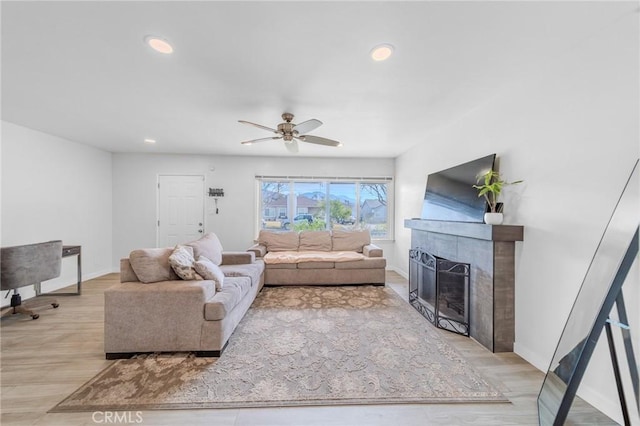 living room featuring ceiling fan, a fireplace, and light wood-type flooring