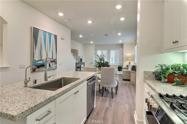 kitchen with stainless steel appliances, white cabinets, a sink, and light stone countertops