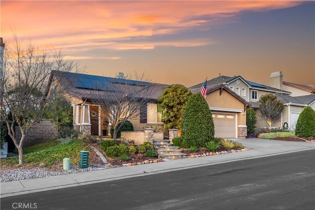 view of front facade with an attached garage, stucco siding, stone siding, aphalt driveway, and roof mounted solar panels