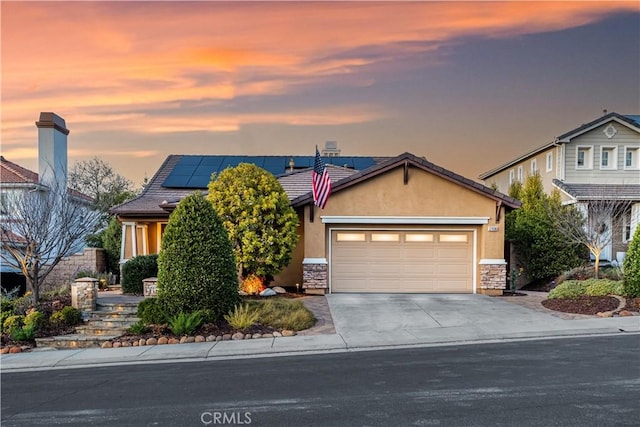 view of front of property with roof mounted solar panels, a garage, driveway, and stucco siding