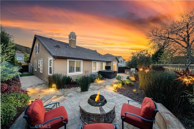 back house at dusk featuring a hot tub, a patio area, and an outdoor fire pit