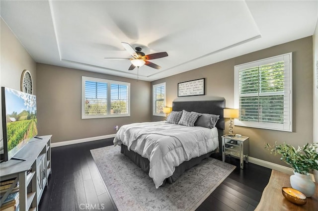 bedroom with ceiling fan, dark hardwood / wood-style flooring, and a tray ceiling