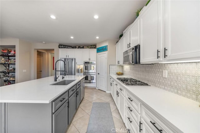 kitchen with stainless steel appliances, white cabinetry, gray cabinets, and a center island with sink