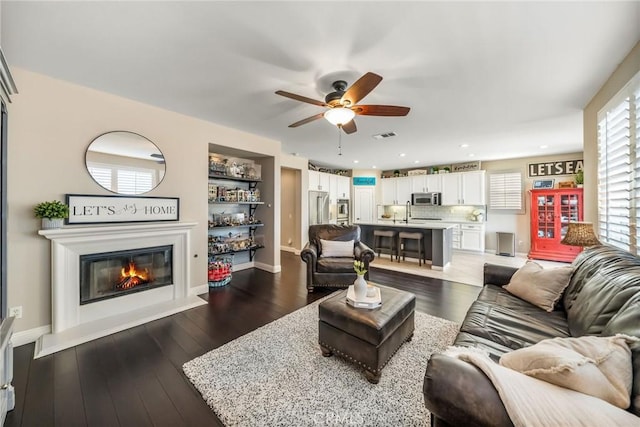 living room featuring sink, dark wood-type flooring, and ceiling fan