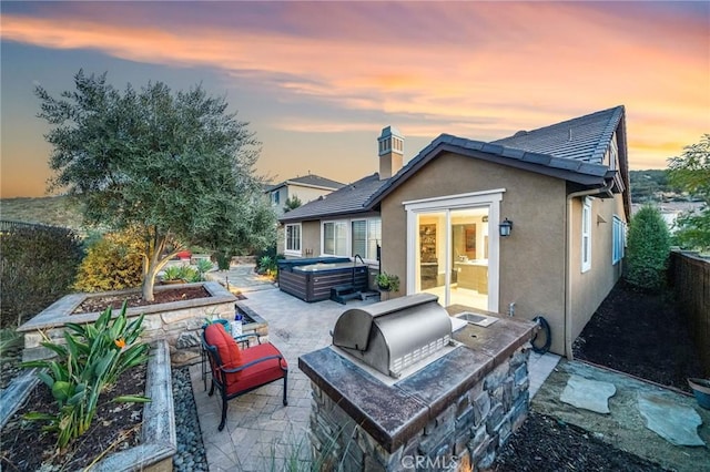 back house at dusk with exterior kitchen, a hot tub, and a patio area