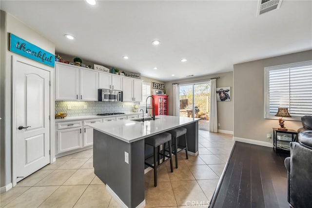 kitchen featuring a breakfast bar, white cabinets, light tile patterned floors, gas stovetop, and a center island with sink