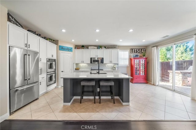 kitchen with light tile patterned flooring, a breakfast bar, a center island with sink, appliances with stainless steel finishes, and white cabinets