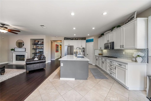 kitchen with stainless steel appliances, a kitchen island with sink, white cabinets, and decorative backsplash