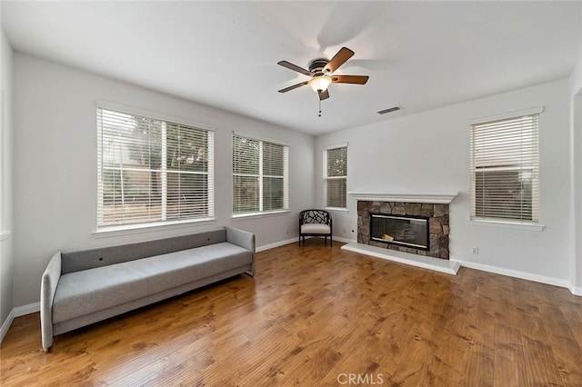 unfurnished room featuring hardwood / wood-style floors, a stone fireplace, and ceiling fan