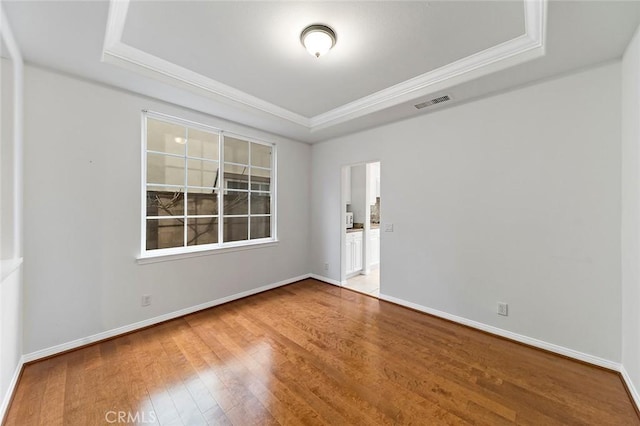 empty room with a raised ceiling, wood-type flooring, and crown molding