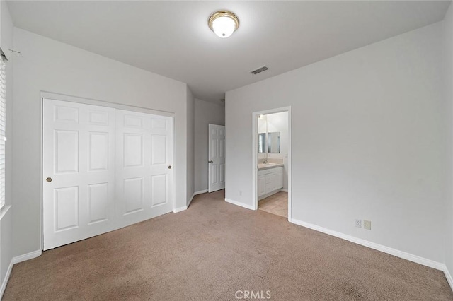 unfurnished bedroom with light colored carpet, ensuite bathroom, and a closet