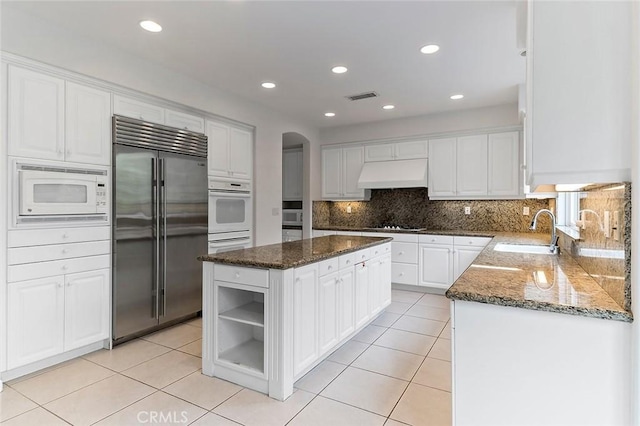 kitchen with sink, custom exhaust hood, built in appliances, a kitchen island, and white cabinets