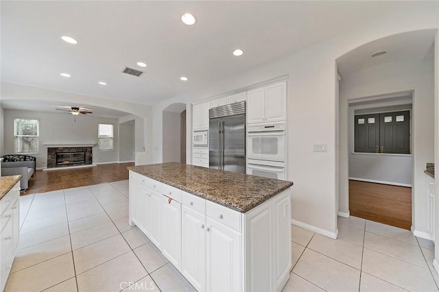 kitchen featuring white cabinetry, built in appliances, light tile patterned floors, a kitchen island, and dark stone counters