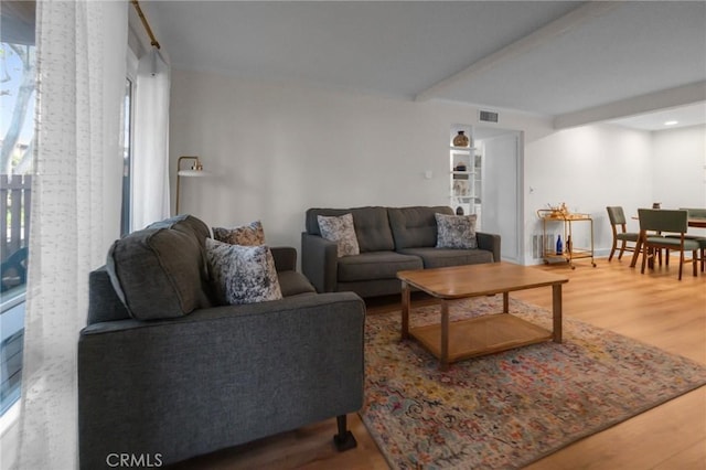 living area featuring visible vents, beamed ceiling, and wood finished floors