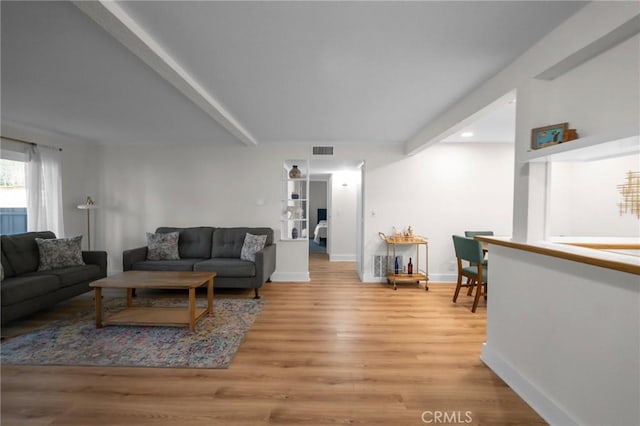 living room featuring light wood-style flooring, visible vents, baseboards, and beamed ceiling