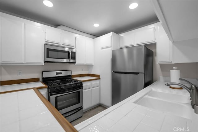 kitchen featuring recessed lighting, a sink, white cabinetry, appliances with stainless steel finishes, and tile counters