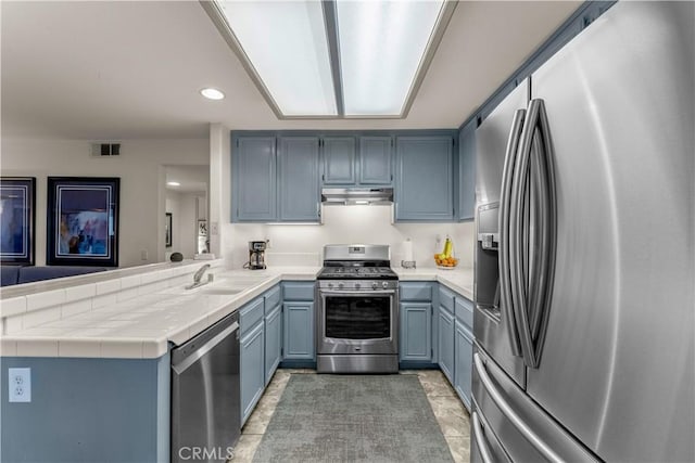 kitchen with sink, tile counters, stainless steel appliances, and kitchen peninsula