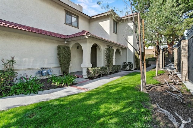 view of property exterior featuring a tiled roof, a yard, fence, and stucco siding