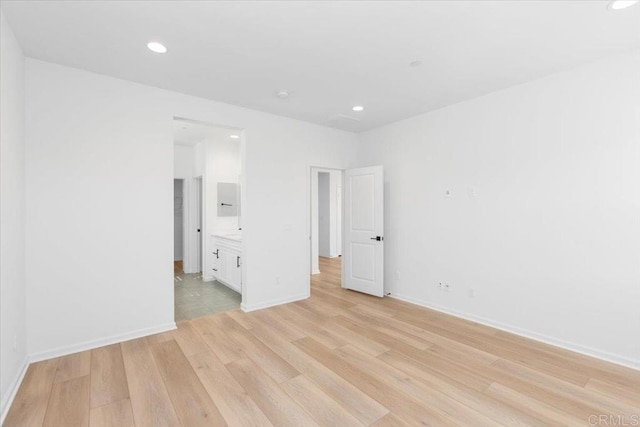 unfurnished bedroom featuring ensuite bathroom and light hardwood / wood-style flooring