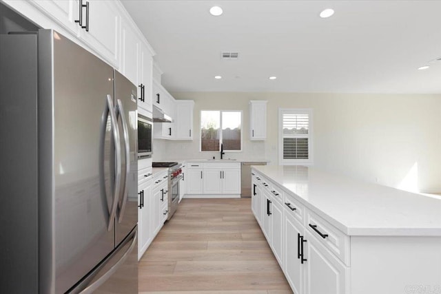 kitchen with sink, appliances with stainless steel finishes, white cabinets, a kitchen island, and light wood-type flooring