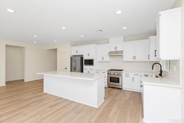 kitchen with appliances with stainless steel finishes, sink, white cabinets, a center island, and light hardwood / wood-style flooring