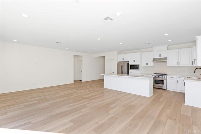 kitchen with a kitchen island, appliances with stainless steel finishes, white cabinetry, sink, and light hardwood / wood-style flooring