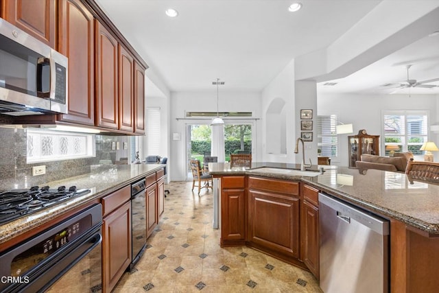 kitchen with sink, tasteful backsplash, hanging light fixtures, appliances with stainless steel finishes, and a kitchen island with sink