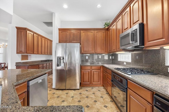 kitchen with appliances with stainless steel finishes, a chandelier, decorative backsplash, and dark stone counters