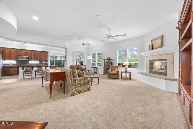 living room with a tiled fireplace, light carpet, and ceiling fan