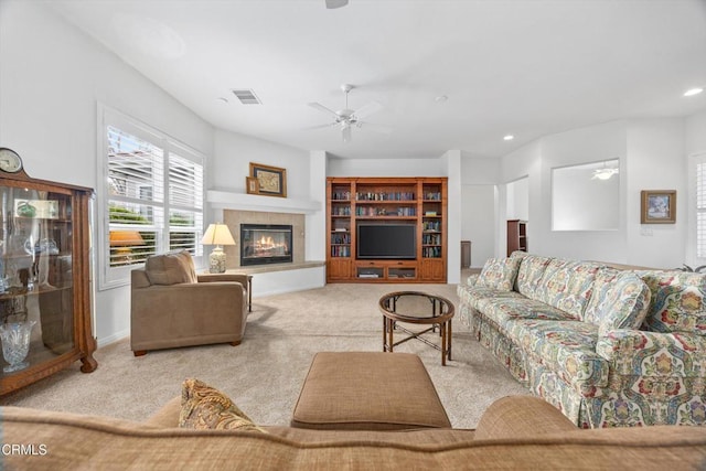 carpeted living room with ceiling fan and a tiled fireplace