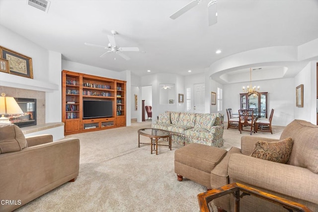 carpeted living room featuring a tiled fireplace and ceiling fan with notable chandelier