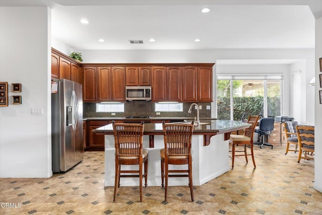 kitchen with appliances with stainless steel finishes, a kitchen island with sink, a breakfast bar area, and backsplash