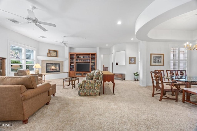 living room featuring light carpet, ceiling fan with notable chandelier, and a tile fireplace