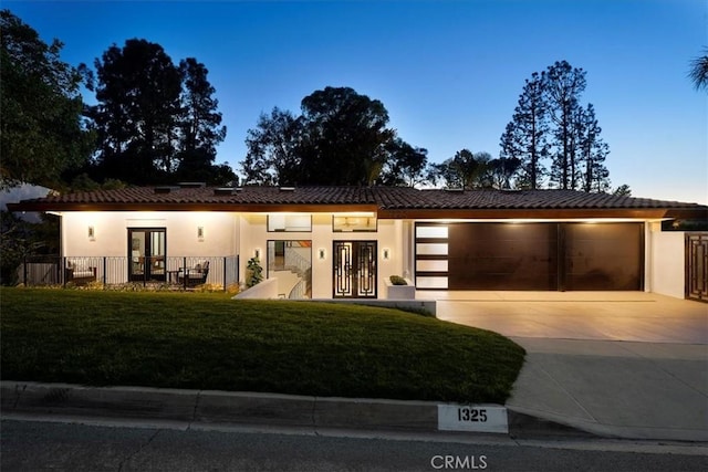 view of front facade featuring concrete driveway, a tile roof, an attached garage, french doors, and stucco siding