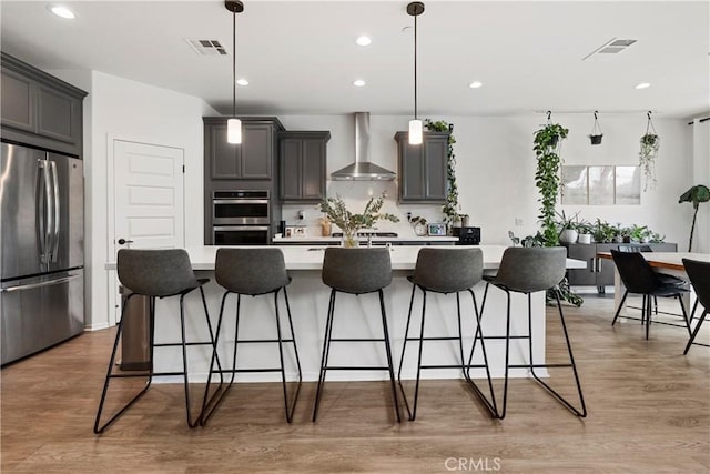 kitchen featuring visible vents, appliances with stainless steel finishes, light countertops, light wood-type flooring, and wall chimney range hood